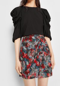 Top nero a maniche a sbuffo abbinato a una gonna a fiori in paisley rossa, blu e nera con un design arricciato e tessuto leggero.