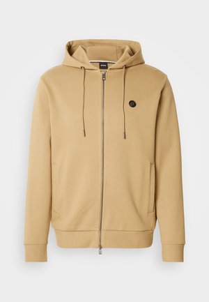 Brązowa bluza z kapturem na zamek wykonana z miękkiego materiału z mieszanki bawełny. Posiada kaptur ze sznurkiem, boczne kieszenie oraz mały logo na piersi.