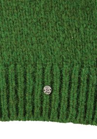 Close-up van groene gebreide stof met ribbelstructuur en een klein rond metalen label gegraveerd met een hart en het woord "Key Largo."