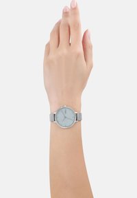 Silbernes Mesh-Armband-Uhr mit einem runden, hellblauen Ziffernblatt. Verfügt über minimalistische Stundenmarkierungen und eine einfache Krone auf der rechten Seite.
