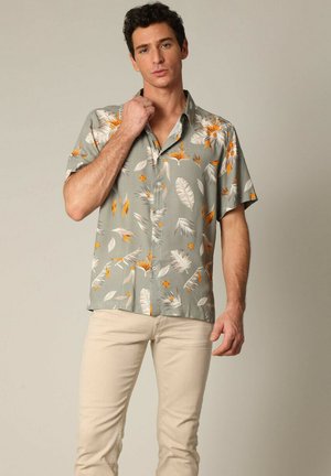Chemise à manches courtes en tissu gris clair, ornée d'un motif de feuilles et de fleurs orange et blanc. Design à boutons avec col.