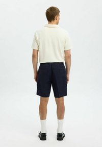 Kortärmad, texturerad krämfärgad pikétröja i kombination med marinblå shorts. Shortsen har en avslappnad passform och två bakfickor med knappstängningar.