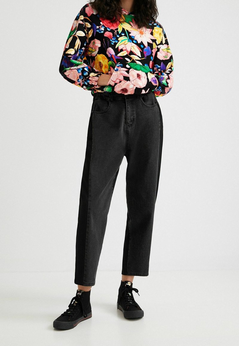 Pantalones de mezclilla negra de tiro alto con un corte relajado, combinados con una blusa larga de manga larga de flores coloridas con puños elásticos y un escote redondo.