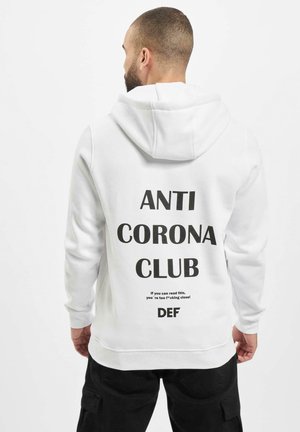 Hvid hættetrøje med sort tekst på ryggen, der står "ANTI CORONA CLUB" samt yderligere budskaber. Har justerbar hætte og ribbede manchetter.