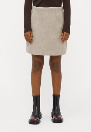 Light grey wool mini skirt with two side pockets, paired with black ankle boots featuring a red accent, shown from the waist down.