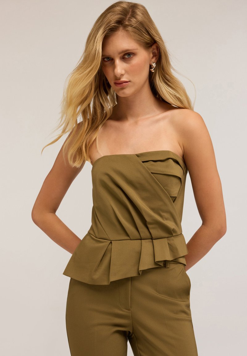 Top senza spalline verde oliva con design plissettato, corpetto a vita stretta e orlo peplum. La texture del tessuto liscia si sposa con la silhouette strutturata.