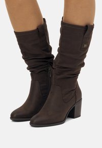 Bottes en tissu marron jusqu'au genou avec un design décontracté, des orteils ronds, des fermetures éclairs sur le côté et un talon épais. Comprend un petit accent de logo.