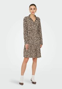 Robe chemise à imprimé léopard avec col boutonné, manches longues et design de jupe à volants ; complétée par des chaussures à motifs et des chaussettes blanches.