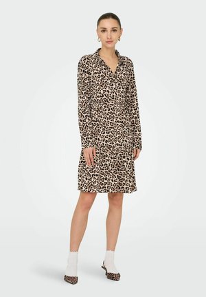 Robe chemise à imprimé léopard avec col boutonné, manches longues et design de jupe à volants ; complétée par des chaussures à motifs et des chaussettes blanches.