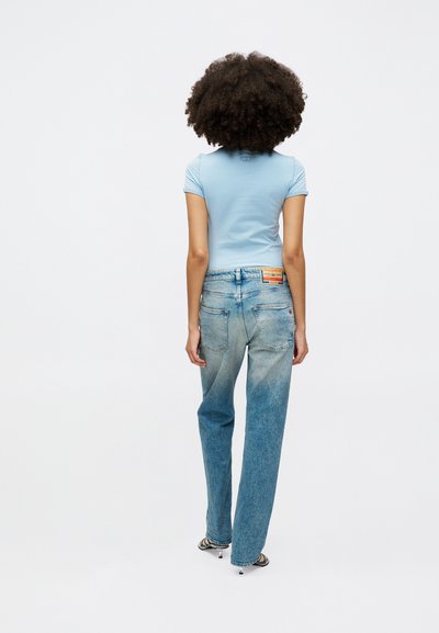 Haut bleu clair à manches courtes associé à un jean bleu clair délavé. Le jean dispose de poches arrière et d'une étiquette sur la taille.