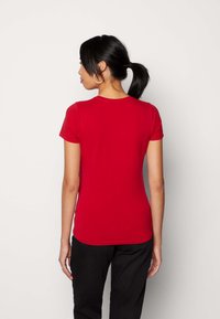 T-shirt rosso a maniche corte realizzato in tessuto liscio. Design aderente con scollatura rotonda. Vista posteriore, che mostra un colore uniforme senza motivi o dettagli.