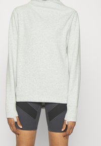 Sudadera gris claro con cuello alto y mangas largas, combinada con pantalones cortos de negro y gris con un diseño ajustado.