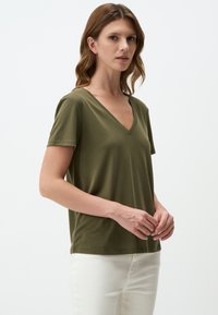 T-shirt verde oliva con scollo a V e maniche corte, realizzato in tessuto morbido. Abbinato a pantaloni bianchi, presenta una vestibilità rilassata.