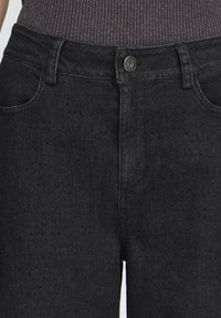 Jeans in denim nero con una superficie strutturata con piccoli fori, design classico con cinque tasche e chiusura con bottone in metallo.