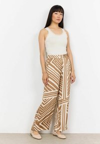 Brown and cream patterned wide-leg trousers with diagonal stripes, made of lightweight fabric. Paired with a light tank top and beige flats.