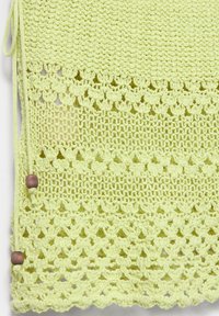 Tissu crocheté jaune-vert avec bords festonnés, motifs floraux et en maille, et cordons noués avec des perles en bois sur fond blanc.