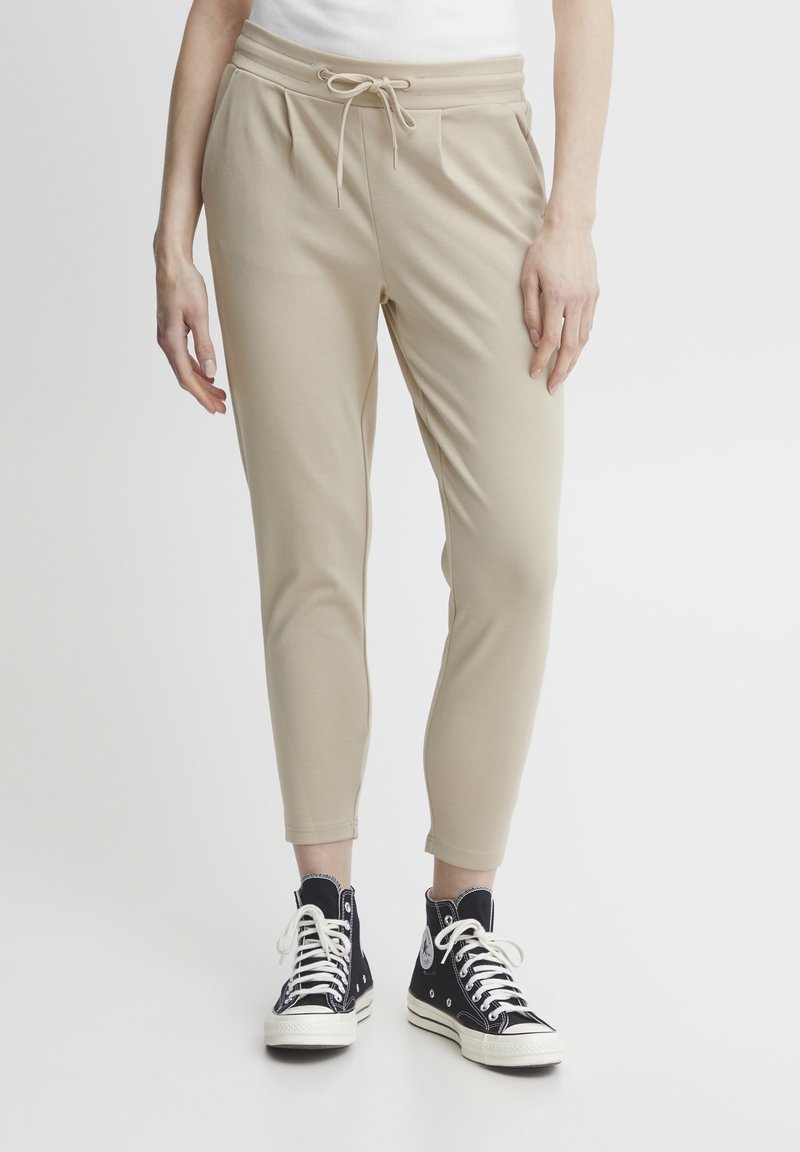 Beiga, lätta joggers med dragsko i midjan, avsmalnande ben och subtila veck, parat med höga svarta sneakers.