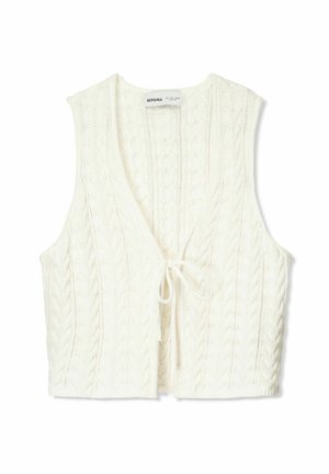 Hvid strikket vest med V-hals, der har kabelstrik tekstur og en snøre lukning foran. Ærmeløst design, kort længde.