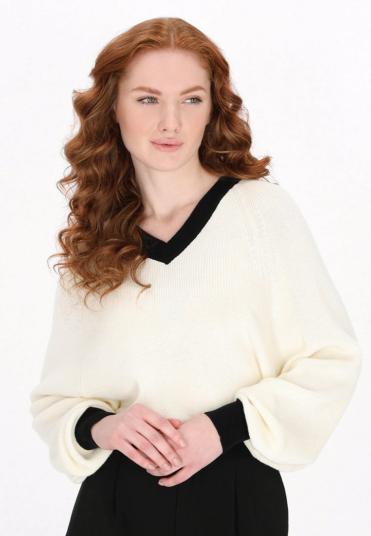 Cremefarbener V-Ausschnitt-Pullover mit schwarzen Akzenten, geripptem Textur und voluminösen Ärmeln. Bietet eine lockere Passform und eignet sich für Freizeitkleidung.