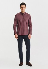 Bordowa koszula z guzikami, z subtelnym wzorem kropek, długimi rękawami i klasycznym kołnierzykiem, zestawiona z ciemnymi spodniami i brązowymi butami.