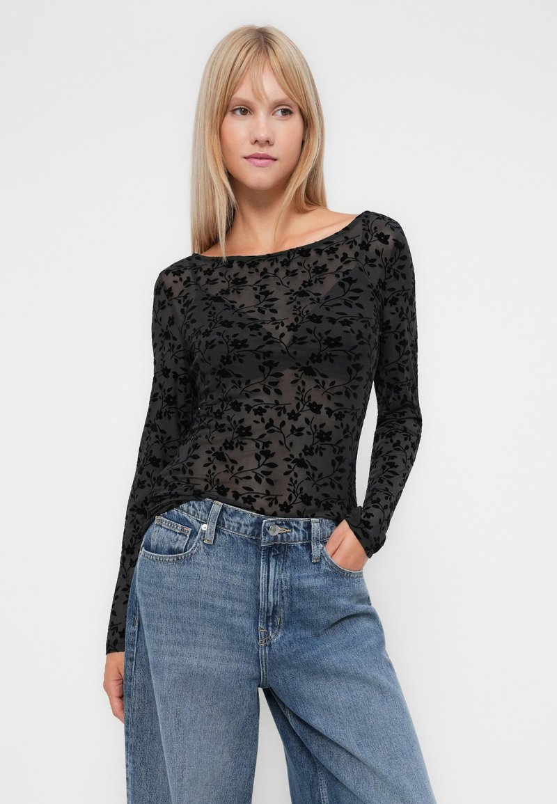 Schwarzes, blumenmusterndes Netzoberteil mit langen Ärmeln und weitem Ausschnitt, kombiniert mit hellblauen, hoch taillierten Jeans. Verfügt über ein transparentes, texturiertes Design.