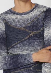 Stickad tröja med ett strukturerat, gradientmönster i marinblått och grått, med metalltrådsackenter och rund halsringning.
