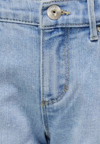 Svetlomodré rifľové nohavice zobrazujúce predný gombík, očko na opasok a vrecko s detailným prešívaním a textúrou látky.