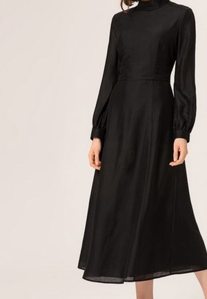 Lange zwarte jurk gemaakt van soepel materiaal, met een hoge hals, lange opgeblazen mouwen en een vloeiende rok die onder de knieën valt.