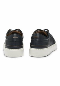 Black leather sneakers with textured finish, white rubber sole, and subtle brown accents. Features a minimalist design and low-cut silhouette.