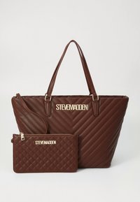 Brun quiltet handlenett med skrå mønstre og gullfarget "Steve Madden"-logo, sammen med en matchende glidelåspose. Begge har en glatt tekstur.