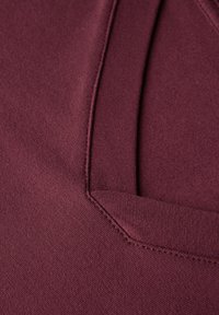 Burgundy stickad tyg med en slät textur, med en V-halsdesign och förstärkta sömmar för hållbarhet. Subtil lyster förbättrar det visuella intrycket.