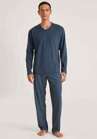 Marineblauwe langemouwen v-hals top met een borstzak, gecombineerd met gestreepte pyjamabroek in blauwe tinten met kleine geometrische ontwerpen.