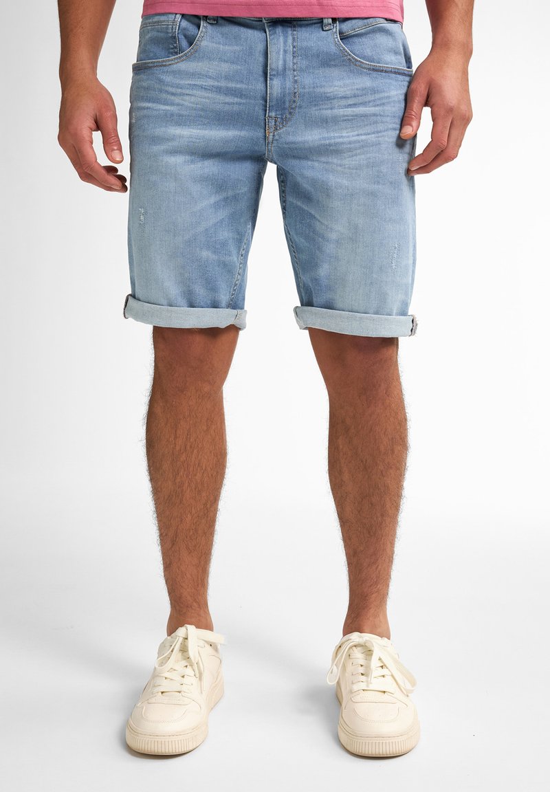 Bermuda in denim azzurro chiaro con risvolti, caratterizzati da una texture leggermente sbiadita e tasche frontali. Abbinati a sneakers bianche con lacci.