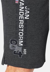 Dunkelgrauer Stoff mit weißem und marineblauem Text, der "JAN ANDERSTORM 84 NOR" liest, und einem kleinen rot-, weiß- und blauem Flaggenemblem oben.