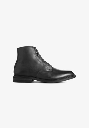 Bottine en cuir noir à lacets, avec un talon bas et empilé, présentée en profil sur un fond blanc.