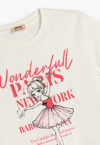 Camiseta de algodón blanca con una ilustración de una bailarina en rosa y negro. El texto dice "Maravillosa París" y "Nueva York". Mangas cortas, cuello redondo.