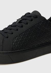 Adidași negri cu brâu din cauciuc texturat, având un model în diamant și șireturi asortate, pe o talpă neagră cu o finisare netedă.