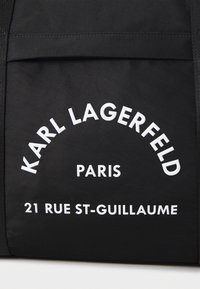 Must must kott, millel on julge valge tekst, mis ütleb "KARL LAGERFELD PARIS" ja "21 RUE ST-GUILLAUME", esitledes puhtat ja kaasaegset disaini.