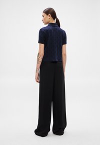 Jūras spēku īsā polo ar teksturētu ģeometrisku rakstu un īsām piedurknēm, kombinēts ar plašām melnām biksēm. Gluda auduma un pielāgota piegriezuma.