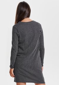 Musta pitkähihainen mekko, jossa on pystysuorat valkoiset raidat, pyöreä pääntie ja rento malli. Valmistettu pehmeästä kankaasta, jossa on sileä pinta.