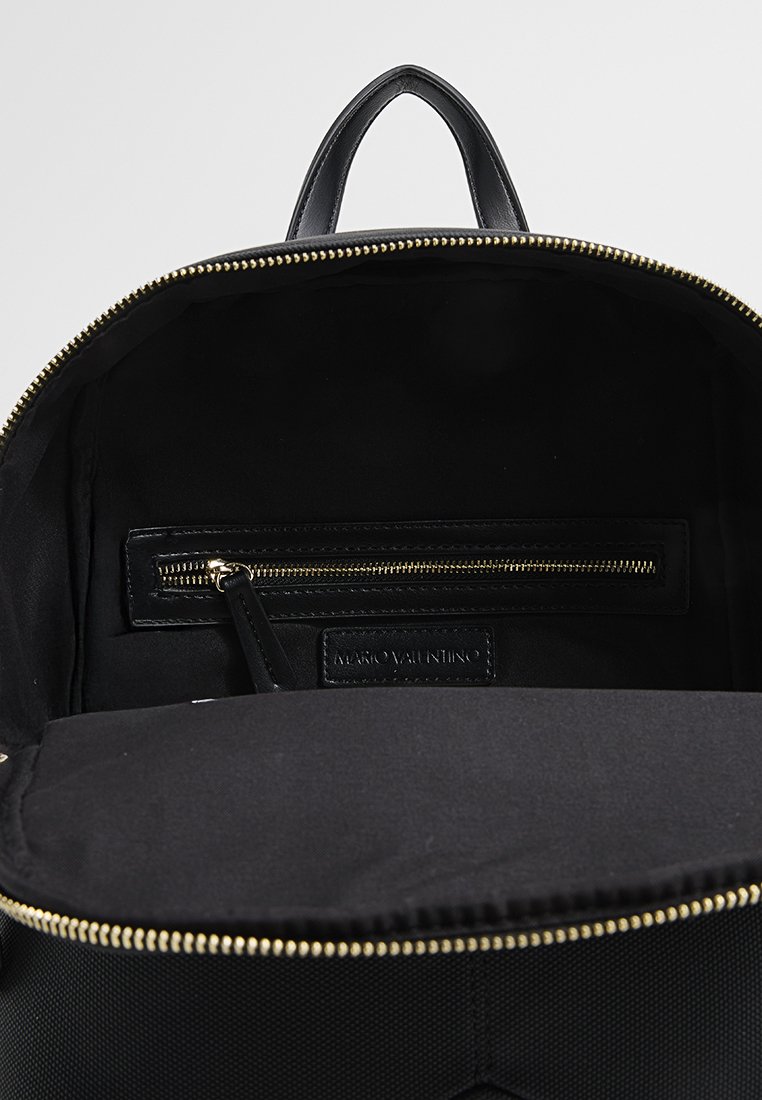 Schwarzer Rucksack mit einer glatten Außenfläche und goldenen Reißverschluss. Das Innere verfügt über eine Stoffauskleidung, eine Reißverschlusstasche und ein Markenlabel.