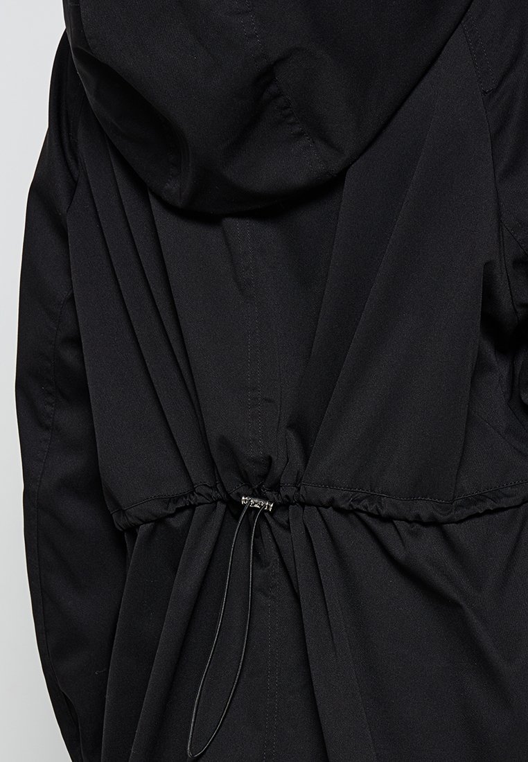 Schwarze Jacke mit einer taillierten Taille und verstellbarem Kordelzug, einer Kapuze und einem glatten, strukturierten Stoff. Schlichtes und funktionales Design.