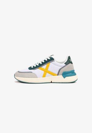 Athletic sneaker in white mesh with gray suede accents. Features a yellow diagonal stripe and teal rubber sole. Classic lace-up design.