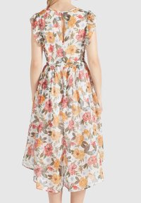 Rückansicht einer Frau, die ein weißes, blumenmusterndes Midikleid mit Rüschensleeves und einer kleinen Aussparung am oberen Rücken trägt.