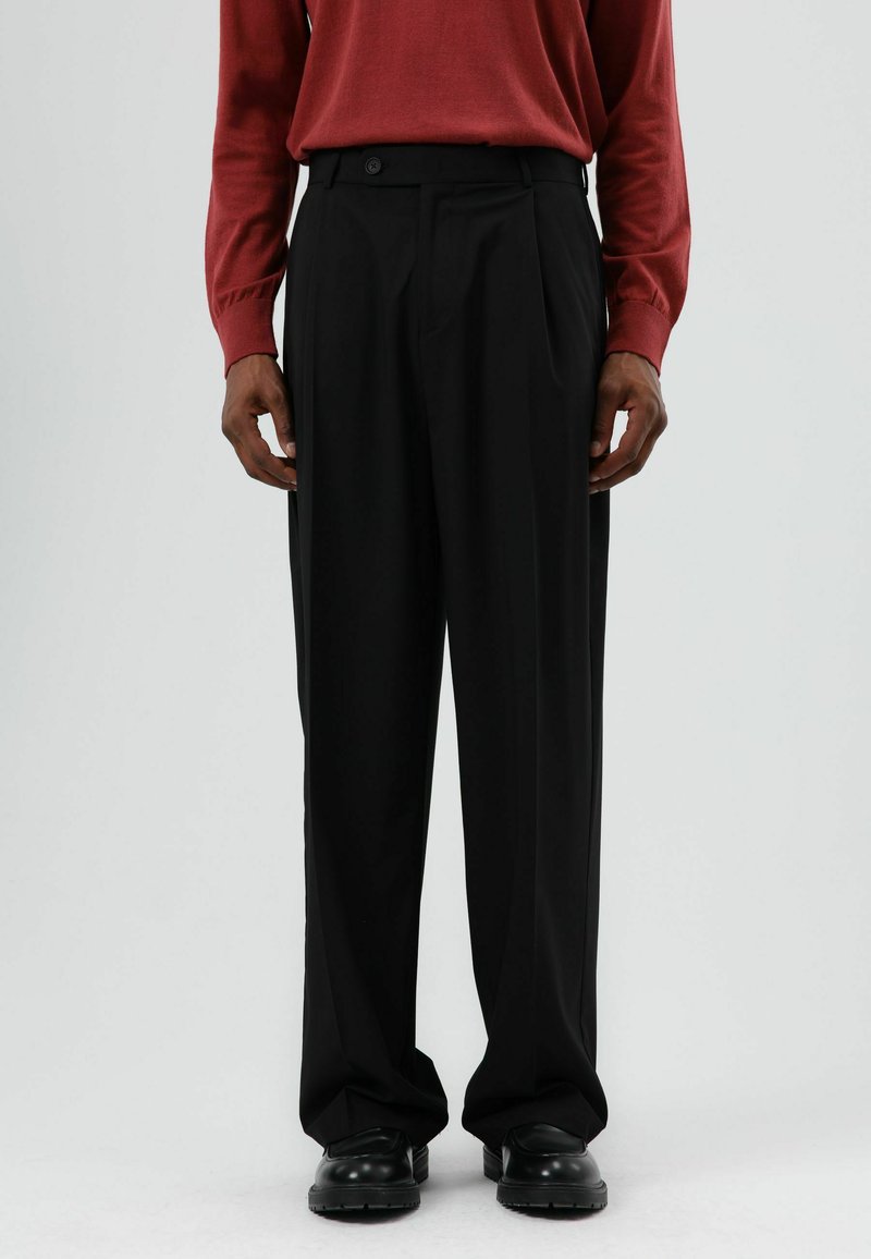 Zwarte geplooide broek met een hoge taille, knoopsluiting, losse pasvorm en een gladde textuur, gecombineerd met een rood gebreide top met lange mouwen.