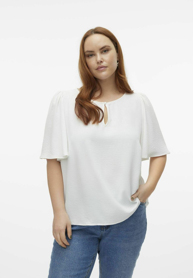 Witte blouse met korte puffmouwen, een ronde halslijn met een keyhole-detail en een zachte, gestructureerde stof. Gecombineerd met een blauwe spijkerbroek.