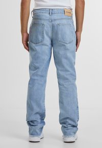 Lys blå denim jeans med en avslappet passform, som har to baklommer og et merke på midjebåndet. Bunnkanten er litt slitt.