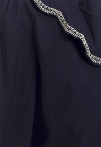 Marinblått tyg med en vågig, vit broderad kant längs övre kanten, med en strukturerad yta och mjuk fall.