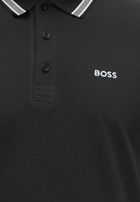Fekete galléros póló fehér csíkos gallérral, három fekete gombbal és fehér hímzett "BOSS" logóval a mellrészen.