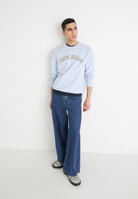 Sudadera de color azul claro con el logo de "Pepe Jeans", combinada con pantalones de pierna ancha a rayas azul y botas grises. Diseño sencillo y corte relajado.